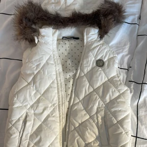 Vit quiltad väst med pälsdetalj - Säljer en snygg vit quiltad väst med fuskpälsdetalj på kragen. 