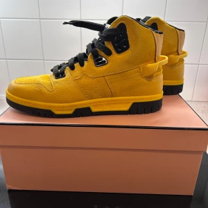 Gula sneakers från Acne Studios - Snygga gula sneakers från Acne Studios med svarta detaljer och snörning. Skorna har en robust sula och är perfekta för en trendig look. De är tillverkade i skinn och har en hög design som ger extra stöd.