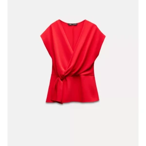Röd omlottopp från Zara - Snygg röd omlottopp från Zara med knytning i midjan. Toppen har en v-ringad design och är ärmlös, vilket ger en elegant och stilren look. Perfekt för att lyfta vilken outfit som helst.
