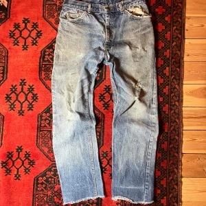 Blå slitna jeans från Lee - Säljer ett par blå jeans från Lee med slitna detaljer och fransig nederkant. De har en klassisk femficksdesign och en bekväm passform. Perfekta för en avslappnad stil.