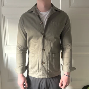 Oliv färgad overshirt från John Henric - Snygg olivgrön overshirt från John Henric i storlek S. Jackan har en klassisk design med knappar framtill och långa ärmar. Perfekt för en stilren look. Jag är 183cm och väger 84kg.