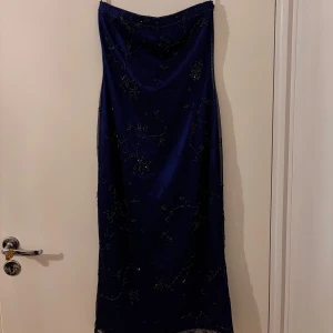 Mörkblå axelbandslös klänning - Elegant mörkblå axelbandslös klänning med vackra broderade detaljer. Perfekt för en speciell kväll.