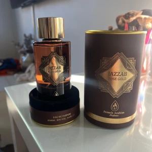 Jazzab Rose Gold Eau de Parfum - Upptäck Jazzab Rose Gold, en elegant Eau de Parfum från French Arabian Perfume. Flaskan har en lyxig brun ton med en gyllene kork och detaljer. Förpackningen är stilren och matchar flaskans design. Perfekt för den som söker en sofistikerad doftupplevelse. Används två gånger.