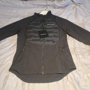 Svart jacka från Peak Performance - HELT NY, OANVÄND!  Nypris 2100kr!                   Snygg svart jacka från Peak Performance med dragkedja och vadderad framsida. Jackan har långa ärmar och en stilren design, perfekt för vår och sommardagar