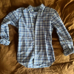 Blå rutig skjorta från Ralph Lauren - Säljer en snygg blå rutig skjorta från Ralph Lauren. Skjortan har långa ärmar och knappar framtill. Perfekt för en stilren look och skjortan är iprincip i nyskick. Nypris 1800kr.