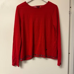 Röd tröja från Armani Jeans - Säljer en snygg röd tröja från Armani Jeans med dekorativa nitar längs kanterna. Tröjan har långa ärmar och en unik design med asymmetrisk öppning framtill. Perfekt för att ge din outfit en färgklick! 💥