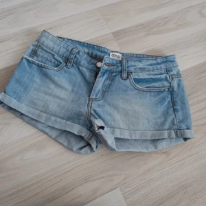 Blå jeansshorts från ASOS - Snygga blå jeansshorts från ASOS med klassisk femficksdesign och uppvikta benslut. Perfekta för en avslappnad sommarlook. De har en knappgylf och bälteshällor för extra stil.
