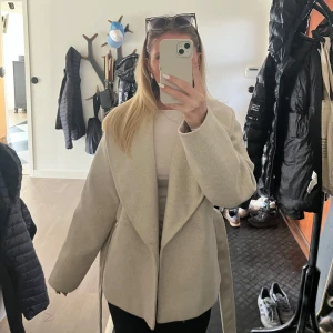 Beige kappa med knytband - Säljer en stilren beige kappa med knytband i midjan. Perfekt för både höst och vår. Knytet runt midjan går även att ta bort! Kappan är nästan aldrig använd, endast en gång vid ett kort tillfälle. 