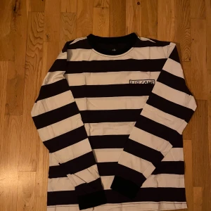 Randig långärmad tröja från Welcome - Säljer en cool randig tröja från Welcome i svart och vit. Tröjan har långa ärmar och ett tryck med texten 'Welcome' på bröstet. Perfekt för en avslappnad stil.