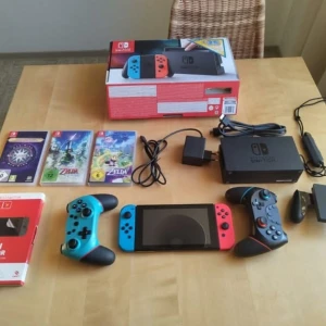 Nintendo Switch med spel och tillbehör - Säljer en Nintendo Switch med blå och röd Joy-Con. Inkluderar tre spel: 'The Legend of Zelda: Breath of the Wild', 'Mario Kart 8 Deluxe' och 'Super Mario Odyssey'. Konsolen kommer med dockningsstation, laddare och extra handkontroller. Perfekt för spelkvällar och gaming på språng!