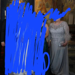 Silverfärgad långklänning med paljetter - Elegant silverfärgad långklänning med glittriga paljetter och fjäderdetaljer på ärmarna. Perfekt för en glamorös kväll. Den har litet kort släp. Nypris: 6000kr använd 1 gång, dragkedja på ryggen. Storlek 46/48