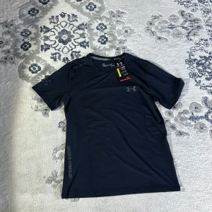 Svart t-shirt från Under Armour - Säljer en svart t-shirt från Under Armour med korta ärmar och logotyp på bröstet. Perfekt för träning eller vardagsbruk. Tillverkad i ett lätt och andningsbart material för maximal komfort. Helt ny oanvänd 