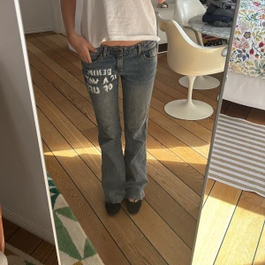 Blå jeans med egengjort tryck - Snygga blå jeans med texten 'DENIM IS A WAY OF LIFE' tryckt i vitt på framsidan. Byxorna har en bootcut-stil och normal passform, vilket ger en avslappnad look. Perfekta för en casual outfit. Jeansen är från Brandy Melville