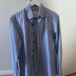 Blå- och vitrandig skjorta från Oscar Jacobson - Snygg blå- och vitrandig skjorta från Oscar Jacobson i bomull och linne. Skjortan har långa ärmar och knappar framtill. Perfekt för en stilren look.