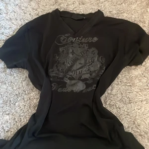 Svart t-shirt med tryck - Säljer en svart t-shirt med ett snyggt tryck på framsidan. T-shirten har en v-ringad hals och korta ärmar. Perfekt för en avslappnad stil.