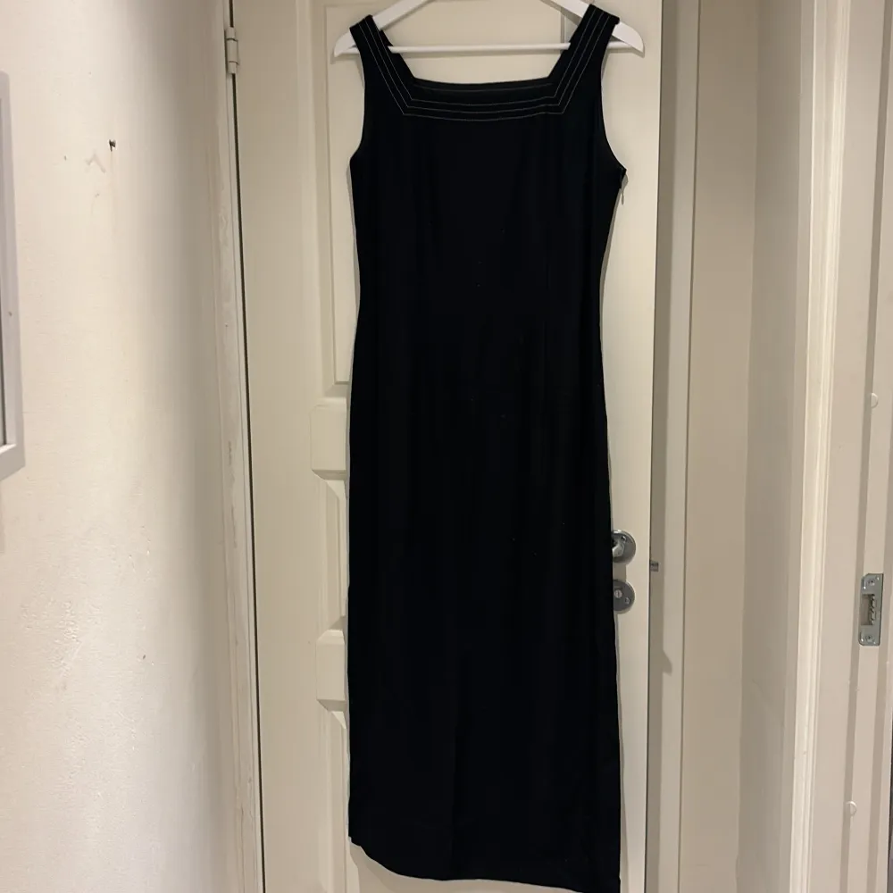 Elegant svart långklänning från TARA med breda axelband och fyrkantig halsringning. Klänningen har en stilren design med kontrasterande sömmar som ger en modern touch. Perfekt för en stilfull look.. Mekot.