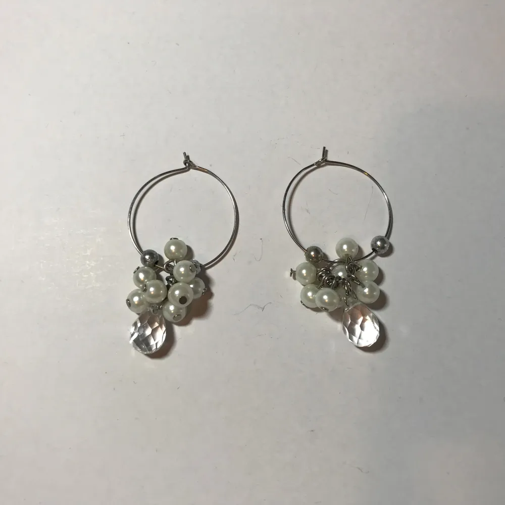 Eleganta örhängen med silverfärgade ringar dekorerade med vita pärlor och klara kristaller. Perfekta för att ge en glittrig touch till din stil.. Asusteet.