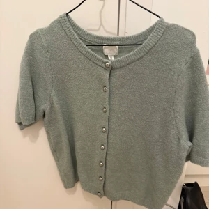 Grön kofta med pärlknappar - Söt grön kofta med korta ärmar och pärlknappar framtill. Aldrig använd och är som ny🌟