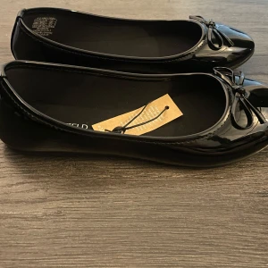 Svarta ballerinaskor med rosett - Snygga svarta ballerinaskor i glansigt material med en söt rosett. Helt nya💗