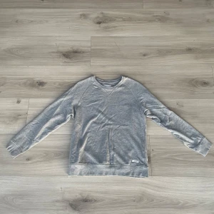 Grå tröja från 157 - Säljer en stilren grå tröja från 157 i storlek S. Tröjan har en v-ringad hals och långa ärmar, perfekt för en avslappnad look. Tillverkad i ett mjukt material som känns skönt mot huden.