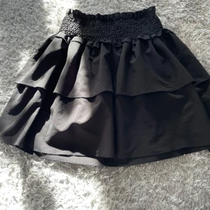 Svart kjol - Snygg svart volangkjol med ribbat i midjan som ger en bekväm och flexibel passform. Kjolen har en volangdesign som ger extra volym, storlek S.