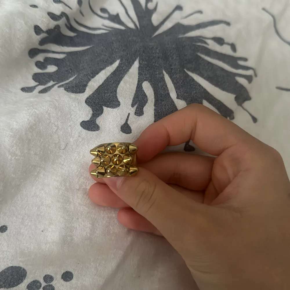 Snygg guldfärgad ring med nitar i en cool design. Perfekt för att ge din outfit en edgy touch. Passar bra till både vardag och speciella tillfällen.. Asusteet.