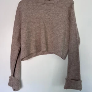 Beige stickad croppad tröja - Stickad tröja med croppad passform. Tröjan har långa ärmar och en rund halsringning. 