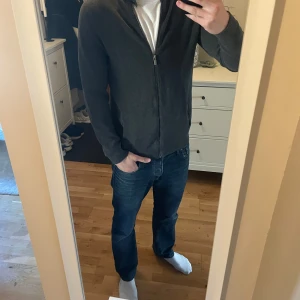 Mörkgrå tröja från Dressmann - Säljer en stilren mörkgrå tröja från Dressmann. Tröjan har dragkedja och knappar vid kragen för extra stil. Perfekt för en avslappnad look. Passar bra till jeans och sneakers.