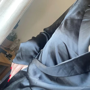 Svart omlottklänning från BikBok - Elegant svart satinklänning från BikBok med en omlott-design. Klänningen har långa ärmar och en klassisk krage, perfekt för en sofistikerad look. Passar utmärkt för både avslappnade och mer formella tillfällen. Längden är till mitten av låren. Otroligt snygg till en kavaj ovan!