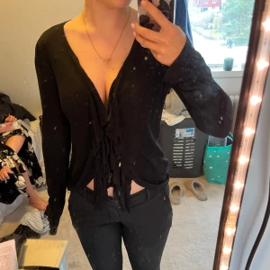 Svart långärmad tröja med volanger - Snygg svart långärmad tröja med volanger framtill. Perfekt för en stilren look. Passar bra till både jeans och kjol.