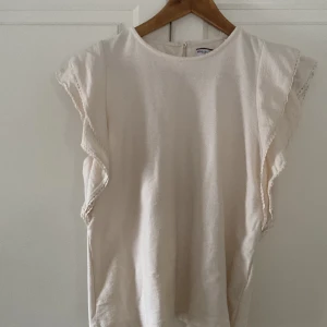 Vit topp från Holly & Whyte - Säljer en stilren vit topp från Holly & Whyte by Lindex. Toppen har korta ärmar med volangdetaljer och är tillverkad i ett mjukt material. Perfekt för en avslappnad men ändå elegant look.
