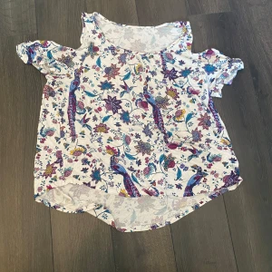 Blommig offshoulder topp från Lindex - Säljer en söt blommig offshoulder topp från Lindex. Toppen har ett färgglatt mönster med blommor i blått, rosa och gult på en vit bakgrund. Perfekt för en somrig look!