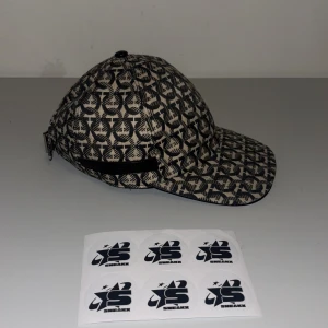 Mönstrad keps med justerbart spänne - Snygg keps med ett unikt mönster i svart och beige. Kepsen har ett justerbart spänne baktill för perfekt passform. Perfekt för att ge din outfit en cool touch.