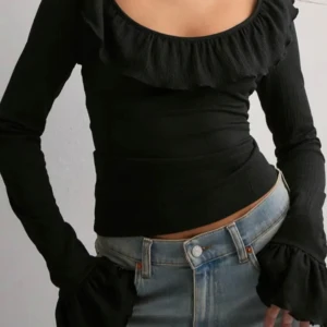 Svart långärmad topp med volangdetaljer - Snygg svart långärmad topp från Nelly med volangdetaljer vid halsringningen och ärmsluten. Perfekt för en stilren look. Toppen har en åtsittande passform. Aldrig använd med prislappen kvar 😊💕