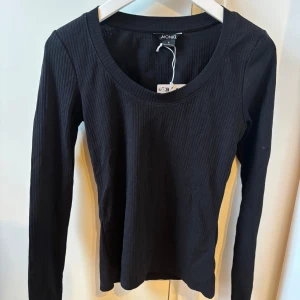Svart ribbad tröja från Monki - Säljer en stilren svart ribbad tröja från Monki. Tröjan har en rund halsringning och långa ärmar, perfekt för lager-på-lager eller som den är. Enkelt och snyggt basplagg för garderoben.
