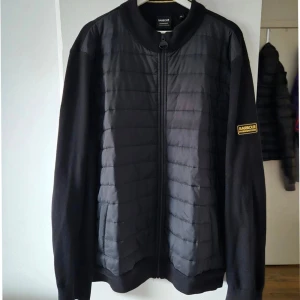 Äkta Barbour - Säljer en stilren svart quiltad jacka från Barbour. Jackan har långa ärmar och en dragkedja framtill. Den är perfekt för kyligare dagar och har en klassisk design med Barbour-logga på ärmen. XXL passar även XL.