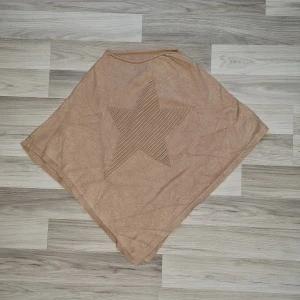 Beige poncho med stjärnmönster - Säljer en snygg beige poncho med ett coolt stjärnmönster i mitten. Ponchon är tillverkad i en mjuk blandning av viskos, bomull och kashmir, vilket gör den både bekväm och stilren. Perfekt för att hålla sig varm och trendig under kyliga dagar. 🌟