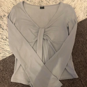 Blå  långärmad topp från Gina Tricot - Säljer en stilren blå långärmad topp från Gina Tricot med en snygg knytdetalj framtill. Perfekt för en avslappnad look. Passar bra till både jeans och kjol. Den är inte mycket använd!