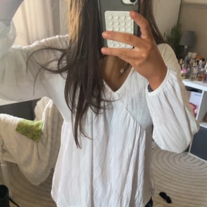Vit blus med v-ringning - Säljer en stilren vit blus med v-ringning och långa ärmar. Blusen har en lös passform och är perfekt för en avslappnad look. Den är tillverkad i ett lätt och luftigt material som ger en skön känsla.