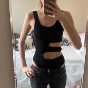 Svart ribbad body - Snygg svart ribbad linnetopp med unika utskärningar i midjan. Den är i ett stretchigt material så passar även större och mindre storlekar. Använd 1 gång och har inga defekter.