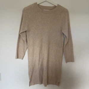Beige stickad klänning med ribbad struktur - Mysig beige stickad klänning med ribbad struktur och rund hals från ZARA. Modellen är rak och har långa ärmar, perfekt för lager på lager. Enkel och stilren design som passar till många olika looks.