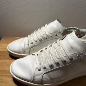 Saint Laurent skor - Unika vita sneakers från Saint Laurent i skinn med coola läppar i blått och rött på hälen. Priset är sänkt då skorna har använts en antal gånger. Skriv gärna om ni har några frågor, och priset kan diskuteras!