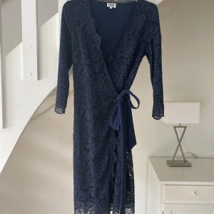 Marinblå spetsklänning Bubbleroom  - Marinblå klänning från Bubbleroom med vacker spets, omlottmodell och knytband i midjan. Klänningen har trekvartsärm och är helfodrad med mjukt polyestertyg. Perfekt för dig som vill ha en elegant och feminin look. Använd 1 gång.