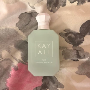 Kayali Yum Pistachio Gelato 33 parfym - Kayali Yum Pistachio Gelato 33 är en parfym i en stilren, ljusgrön flaska med matt finish och vit, multifacetterad kork. Flaskan har en modern, fyrkantig form med mjuka kanter och tydlig logotyp framtill. Perfekt för dig som gillar unika och söta dofter.