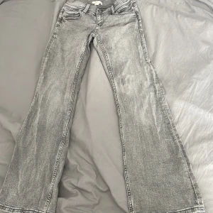 Grå bootcut jeans från Gina Tricot - Snygga grå jeans från Gina Tricot med bootcut passform och cool stjärndetalj på bakfickan. Jeansen har klassisk femficksdesign, dubbla knappar i midjan. Perfekta för dig som gillar en avslappnad men trendig look.