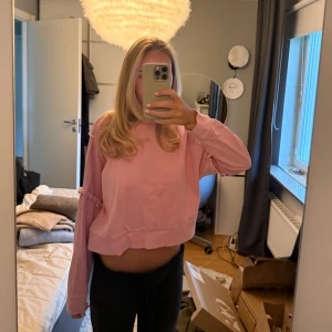 Croppad rosa sweatshirt med volang - Säljer en croppad rosa sweatshirt med volangdetaljer på ärmarna. Tröjan har loose passform och långa ärmar med ribbade muddar. Perfekt för dig som gillar en chill och trendig stil. Materialet känns som mjuk bomull och passar bra till jeans eller mjukisbyxor.