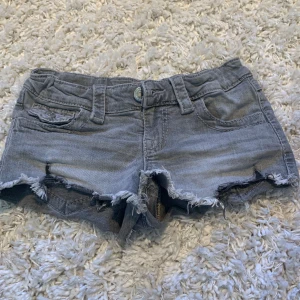 Grå jeansshorts från Gina Tricot - Snygga grå jeansshorts från Gina Tricot med fransiga kanter och slitna detaljer. Klassisk femficksmodell med knapp och dragkedja framtill samt bakfickor med knapp. Perfekta för en chill sommardag. Priset kan diskuteras och om man vill ha mer bilder så kontakta mig här på plick! Kostnaden av frakten står även köparen för💗💐🌺