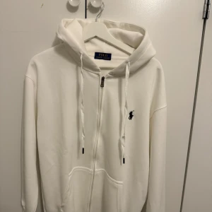 Vit och svart hoodie från Polo  - Två hoodies från Polo , en i vit och en i svart. Båda har dragkedja framtill, huva med snörning och klassisk Polo-logga broderad på bröstet. Tillverkade i mjuk bomull, med långa ärmar och praktiska fickor framtill. Perfekt för chill dagar eller när du vill ha en clean look.