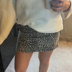 Leopardmönstrad kortkjol i jeans - Säljer en snygg kortkjol med leopardmönster i grå och svart ton. Kjolen är gjord i jeansmaterial och har en rak passform som sitter normalt på kroppen. Perfekt för dig som vill sticka ut med ett coolt djurmönster.