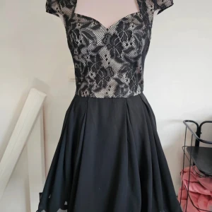 Svart spetsklänning från Chi Chi London - Supersnygg svart kortklänning från Chi Chi London med blommig spets upptill och öppen rygg. Kjolen är utsvängd och materialet är 100% polyester. Perfekt för dig som vill sticka ut med en elegant och ungdomlig look.